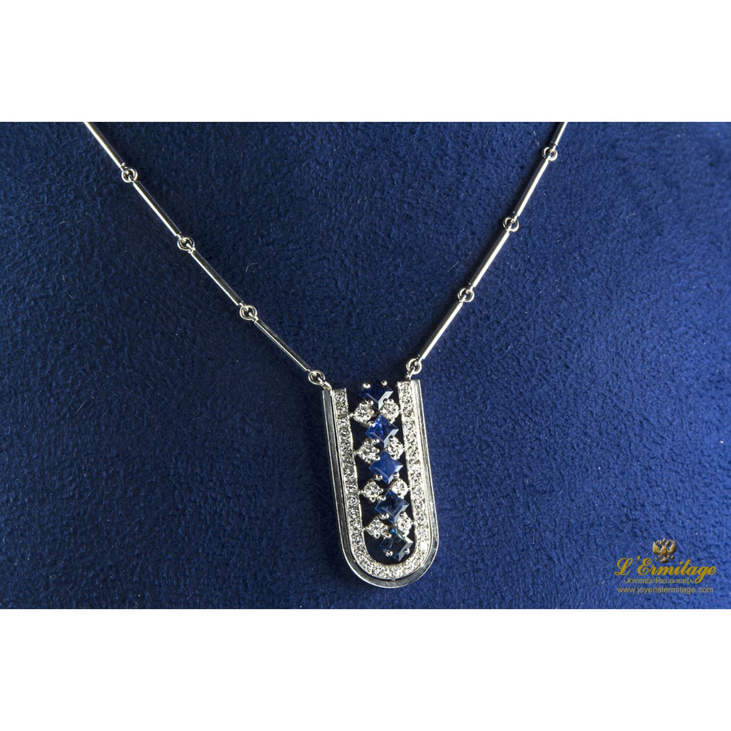 Collar de barras cilíndricas realizado en oro blanco. Presenta colgante con zafiros y brillantes.