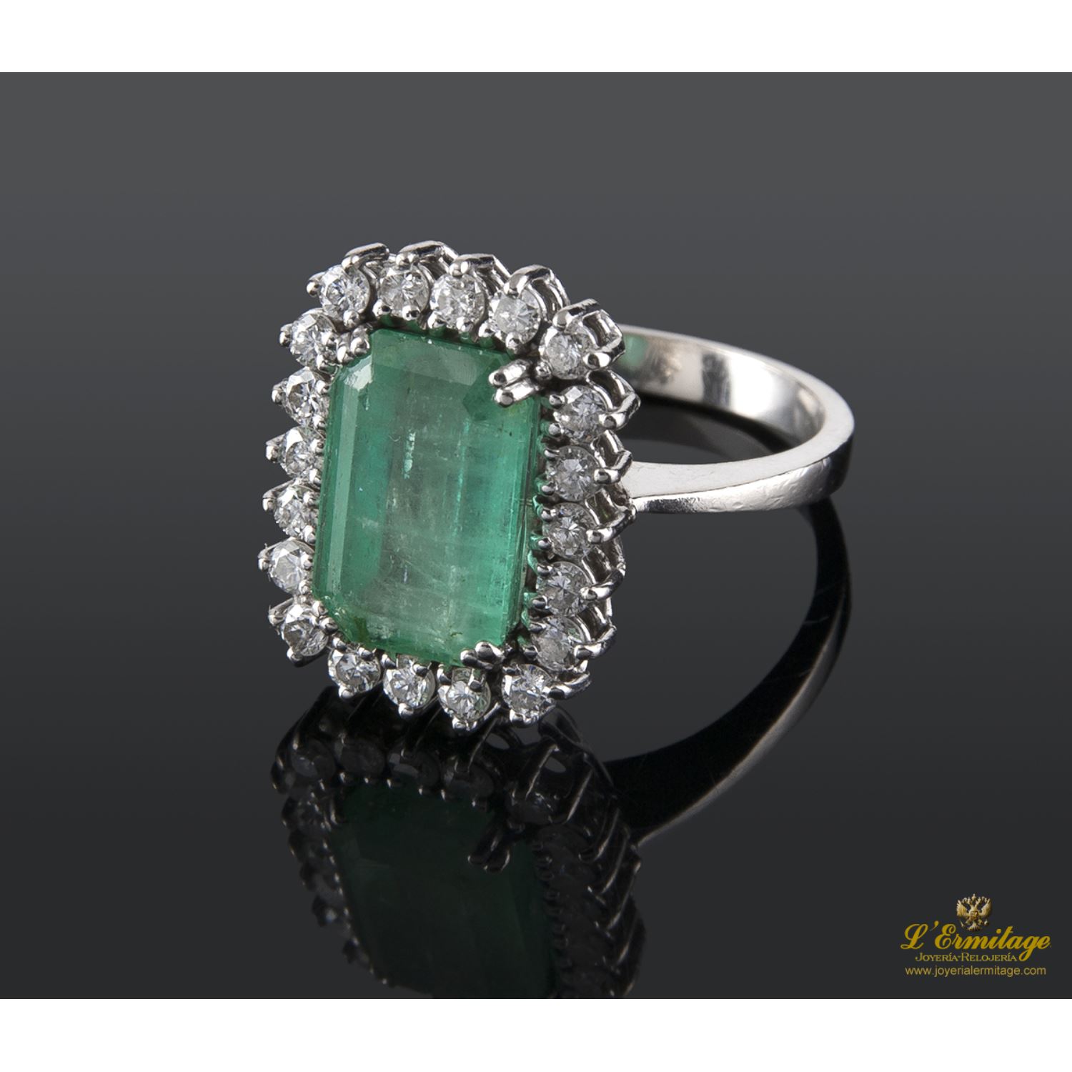 Sortija realizada en oro blanco. Presenta una esmeralda natural con orla de brillantes.
