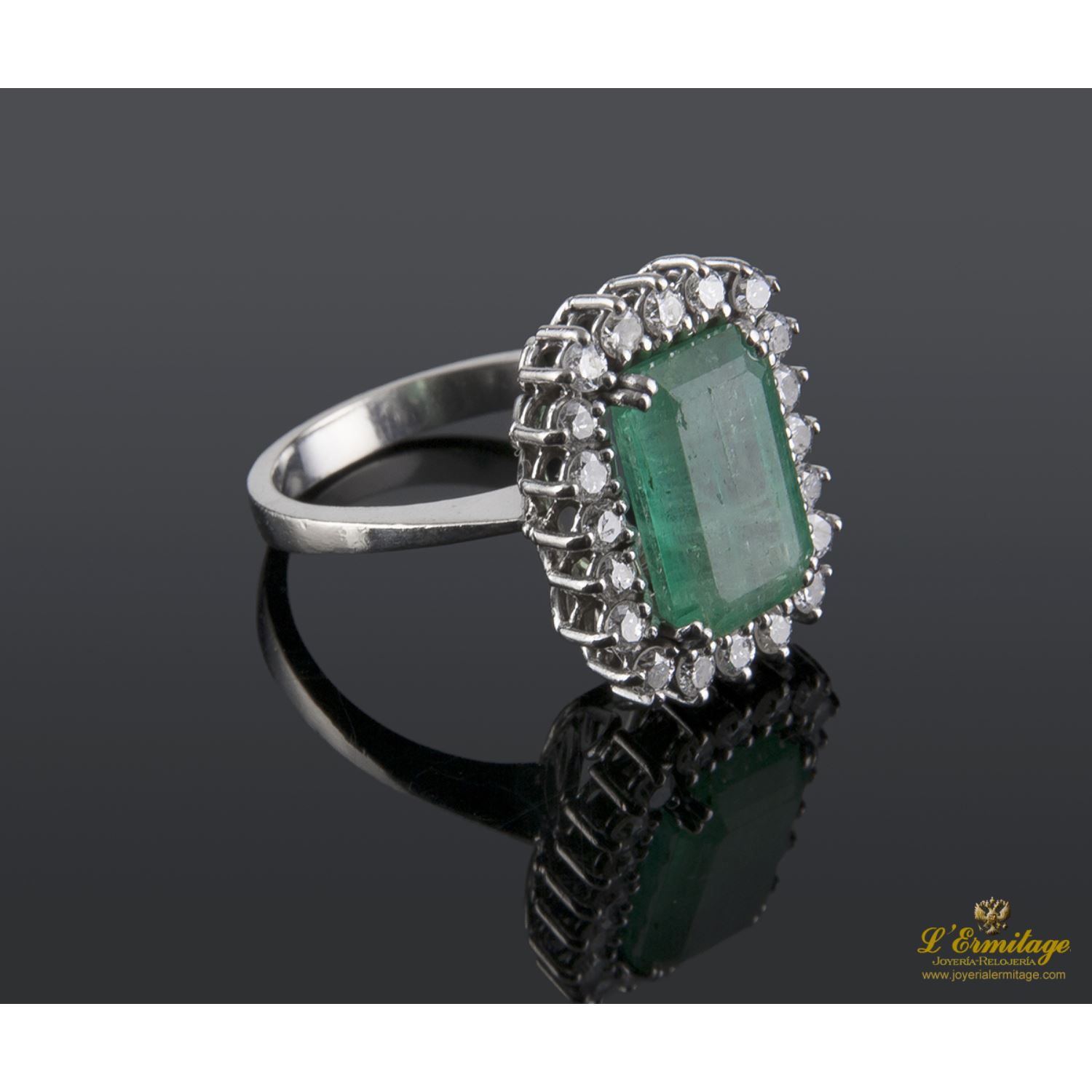 Sortija realizada en oro blanco. Presenta una esmeralda natural con orla de brillantes.